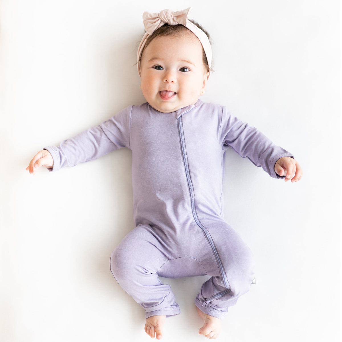 Infant wearing Ziippered Romper in Taro with a headband in Blush