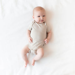 Baby laying on an off-white surface wearing Kyte Baby Bodysuit in Oat