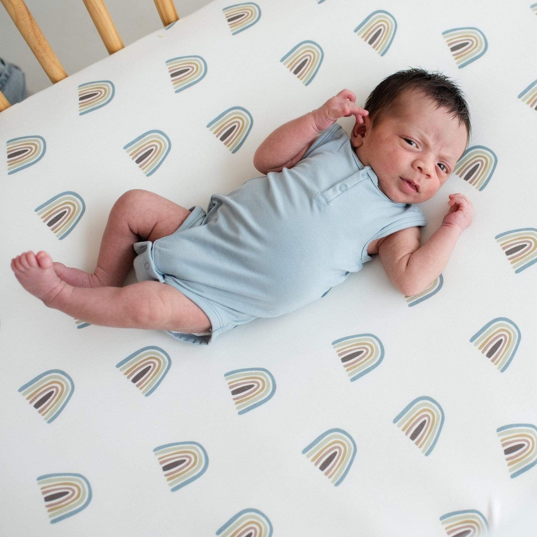 Newborn wearing Kyte Baby Sleeveless infant Bodysuit in Fog while laying in a crib