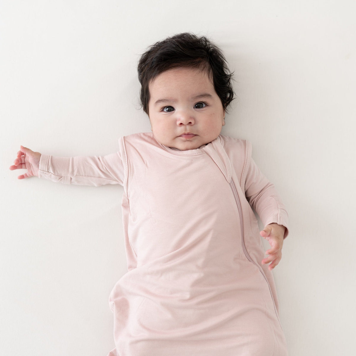 Baby staring straight on wearing Kyte Baby Sleep Bag 0.5 in Blush 