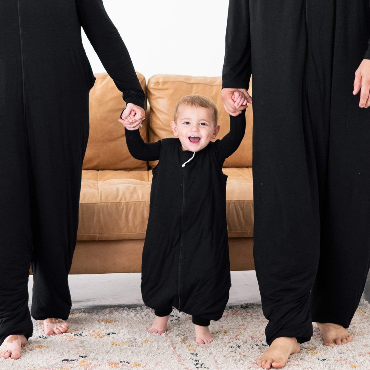 Toddler between two adults in a Sleep Bag Walker in Midnight 1.0. He is holding the adults' hands and they are also in  matching Adult Sleep Bag Walkers