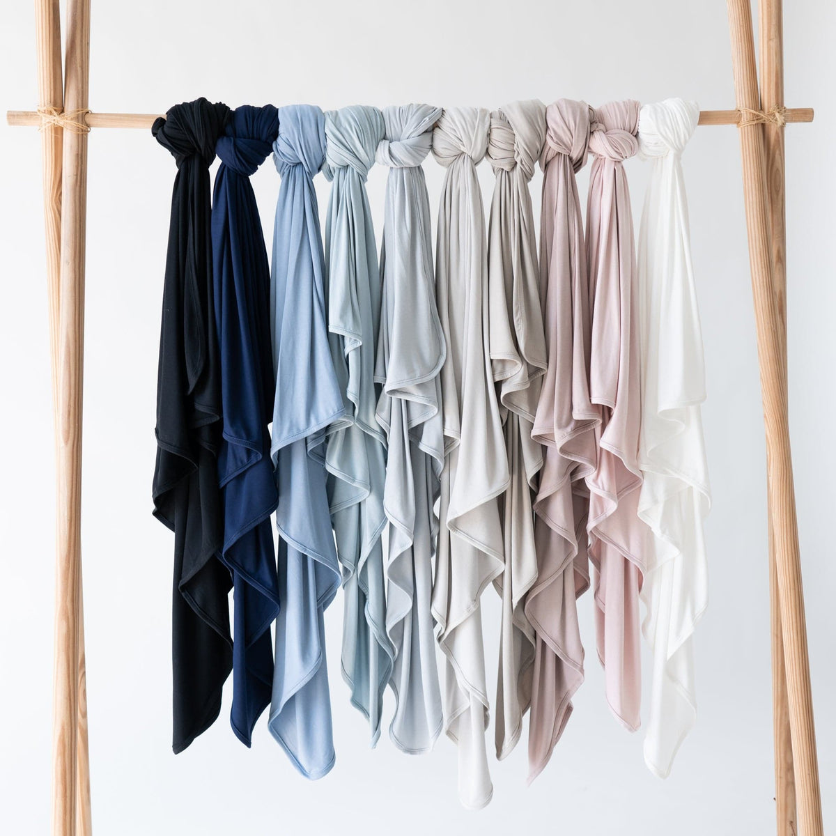 Kyte Baby Swaddle Blankets in multiple core colors hanging on a wooden rack 