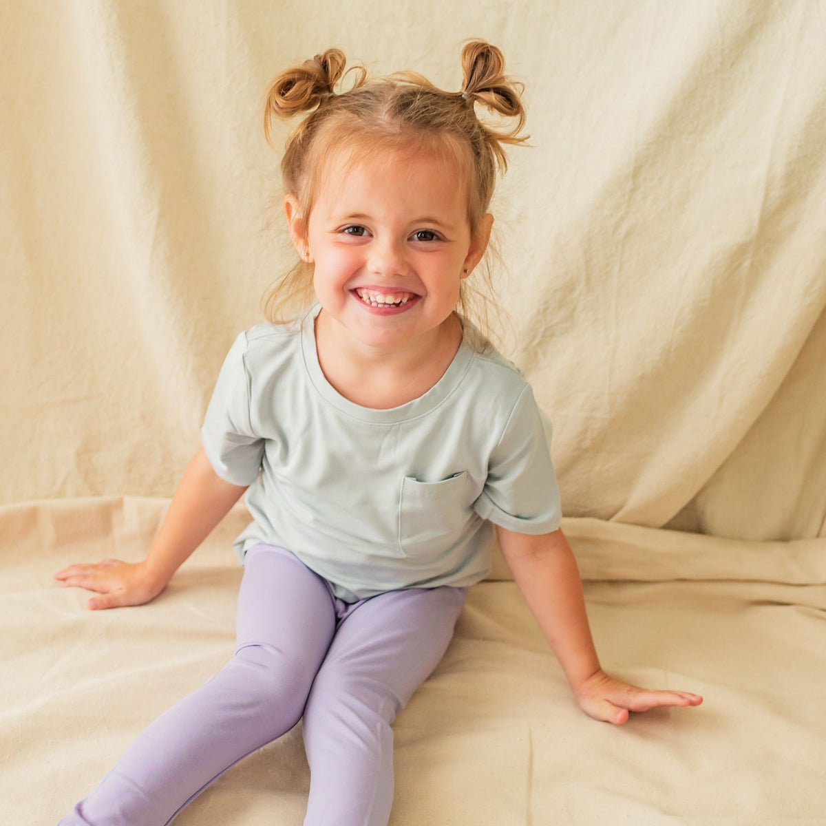 Sitting child smiling and wearing Toddler Leggings in Taro 