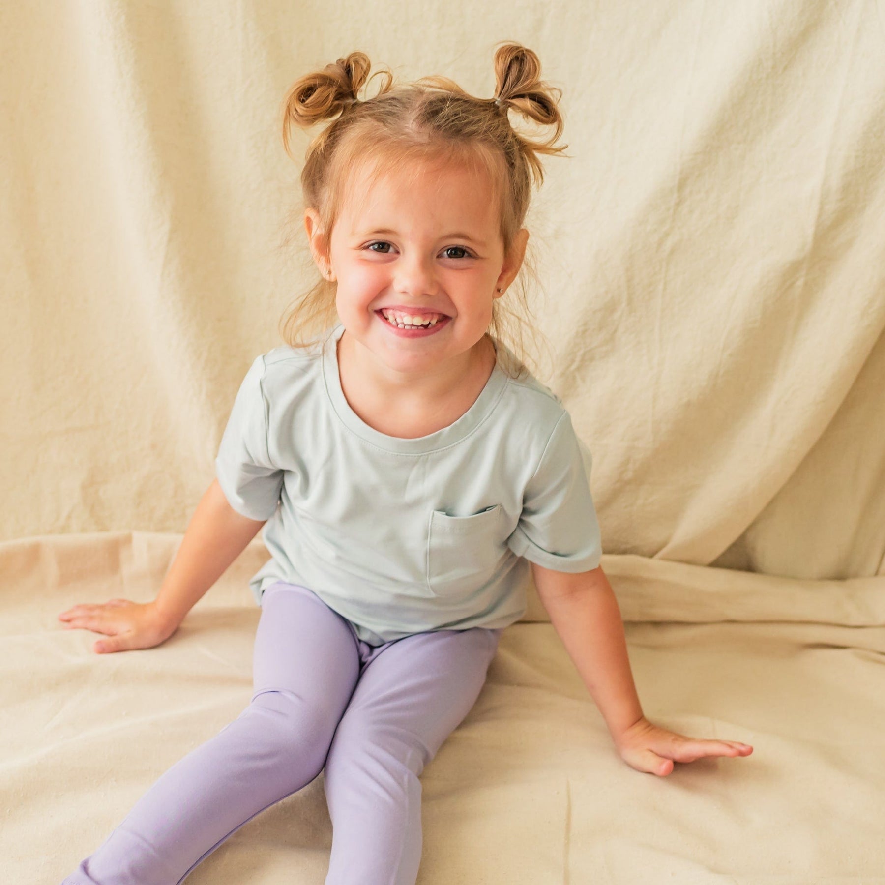 Sitting child smiling and wearing Toddler Leggings in Taro 